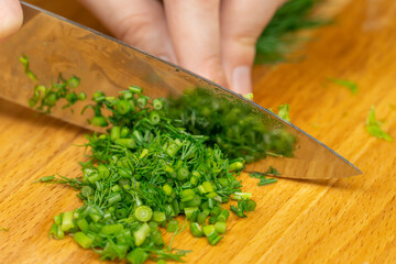 Women's hands cut green dill with a knife on a wooden Board close up