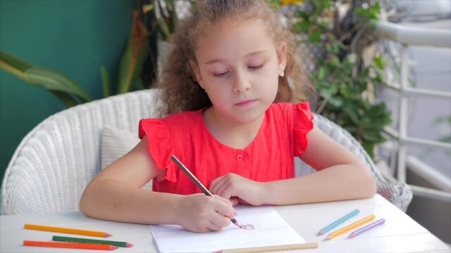 Cute small little girl artist playing alone drawing coloring picture with at home relaxing sits in house and paints on paper use colour pencils.Child draws focused children elementary education