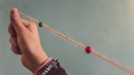 Selective focus shot of two small beads on a thread held straight by a person's hand
