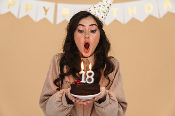 Image of young woman in party cone blowing out candles on birthday cake