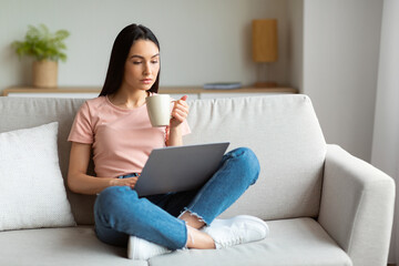 Girl Using Laptop Having Coffee Sitting On Couch At Home