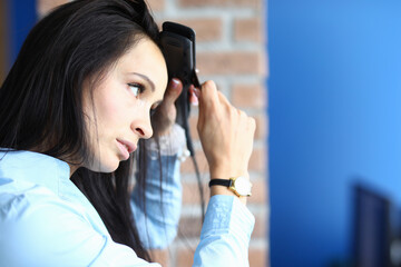 Portrait of woman using straightener on brunette long hair. Cares about hair. Hairdo. Female person with wrist watch. Beauty salon and hairstyle concept