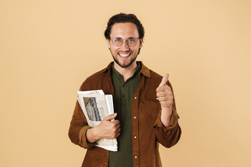 Image of excited unshaven man showing thumb up while holding newspapers