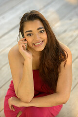 Fototapeta premium Happy young beautiful Indian woman talking on the phone while sitting on wooden floor