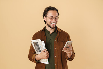 Image of smiling man using mobile phone while holding newspapers