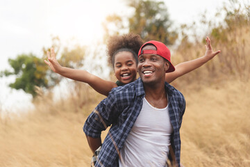 African Father smiling having fun and giving piggyback ride to daughter