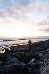 Old man on the rocks looking at the sea at sunset