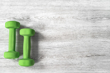 Green dumbbells on a wooden background for fitness classes. Space for text.