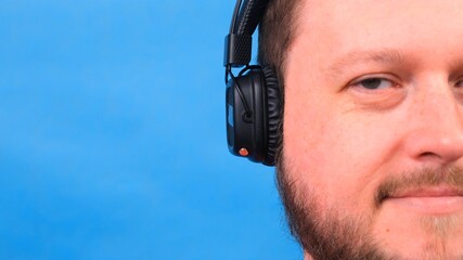 Bearded funny smiling cute fat man in a pink T-shirt listens to music and dances on a blue background, close-up, copy space.