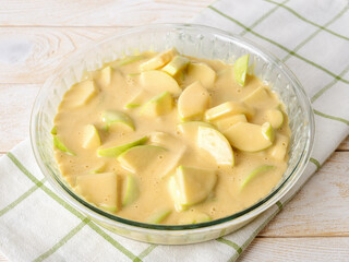 Raw apple pie before baking. Glass baking dish with sliced sour green apples poured a thick dough of eggs, sugar and wheat flour. Easy recipe for homemade baking.