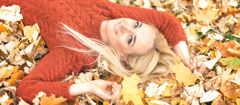 Beautiful young caucasian woman lying down on yellow leaves looking at camera in Autumn Park - Powered by Adobe