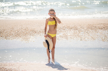 Beautiful girl alone on the beach in a medical mask. A crisis. How to wear a mask when traveling. Family content. Child isolated on the beach. Keep your distance. Beautiful long-haired girl in a swims