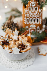 Delicious homemade baked gingerbread house with white icing. Rustic style, white wooden background, candles and christmas lights as decor. Cozy home atmosphere, festive mood, holiday inspiration
