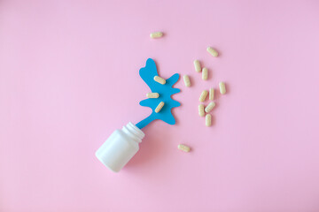 White pill packaging with blue paper splash on pink background. Medicine concept. 