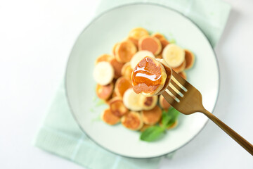 Pouring honey on homemade tiny cereal pancakes on white background. Close up.