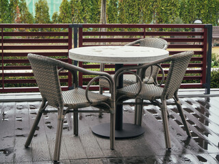 Wicker chairs stand near the round table on the wet wooden floor of a street cafe. Noise effect added