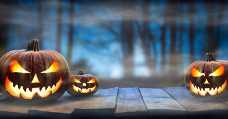 Three spooky halloween pumpkins, Jack O Lantern, with evil face and eyes on a wooden bench, table...