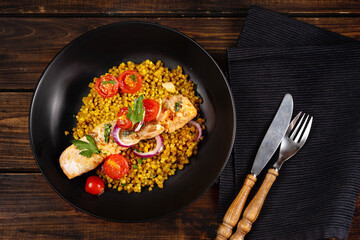 Top view of a black plate with curried green buckwheat, cherry tomatoes and prepared salmon fillet
