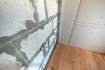 Unfinished brick wall in a room under construction prepared for drywall plates frame installation.