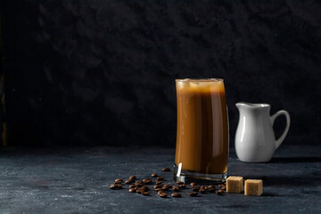 Ice coffee frappe in tall glass. Cool summer drink on a dark background in low key. A stream of milk pours into the coffee. Close up, copy space for text