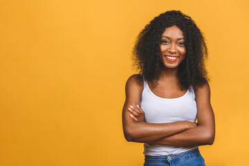 Portrait of beautiful positive african american black woman standing with arms crossed isolated over yellow background.