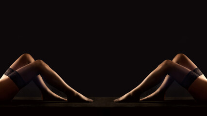 Legs of two women in black stockings  in front of black background