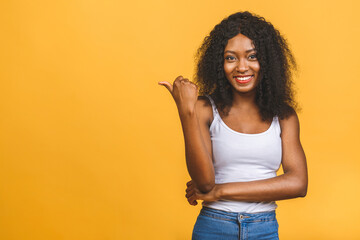 Portrait of a happy young african american woman pointing fingers away at copy space isolated over yellow background.