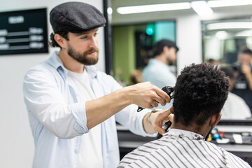 Fototapeta premium . Male beauty treatment concept. Smiling young African guy getting new haircut in barber salon. Portrait of barbers client