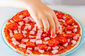 Process of cooking homemade pizza by child. Step 4 kid's hands spreads slices of cherry tomatoes on a dough. Step by step instruction. Children chef concept