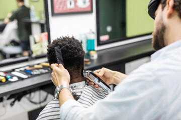 Professional barber makes new haircut with electric shaving machine. Young black man recevie new haircut in barbershop. Male beauty treatment in close up.
