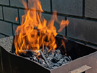 A vibrant orange barbecue flame soars over burning coal