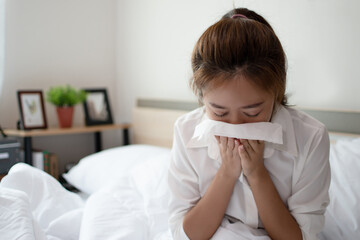 Young business woman is sick and sneezing heavily on the bed. She can't work.