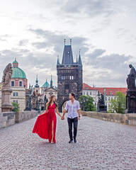 Couple walking during sunrise on Charles Bridge in Prague. Red dress.