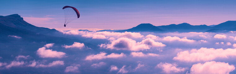 Paraglider silhouette flying above the clouds