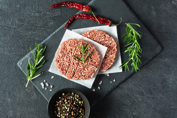 Raw burger cutlets made from minced fresh meet with rosematy and chili on a slate board top view.