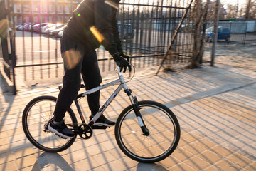 A man in a black tracksuit quickly rides a bicycle in sunny weather. A bicycle cyclist rides on paving slabs in bright sunny weather.