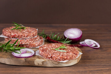 Raw burger cutlets made from minced fresh meet with spices and herbs on wooden background.