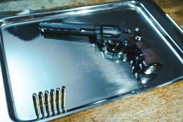 Air gun with bullets lies on a metal tray close-up. Pneumatic revolver with gold cartridges lies on...