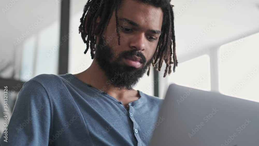 Canvas Prints A close-up view of a handsome african american man is using his silver laptop computer sitting in the living room at home