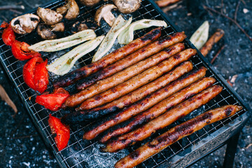 Many long sausages with mushrooms, tomatoes and grilled bell pepper. Cooking vegetables on charcoal. Food in nature. Picnic..