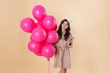 Obraz na płótnie Canvas Image of confused woman using cellphone while posing with pink balloons