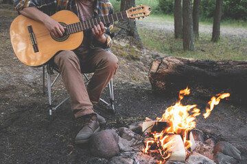 camping in the woods. man plays the guitar by the fire in nature. summer camping. relaxation in...