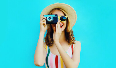 Summer portrait happy smiling young woman with retro camera wearing a summer straw hat on blue background