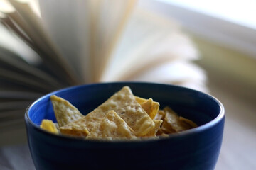 Bowl of tortilla chips and open book on a table. Selective focus.