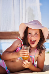a little girl lies on the beach and drinks juice