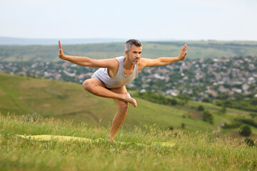 Sporty man doing yoga practice on mountain top. Peaceful guy enjoying his training surrounded by beautiful nature