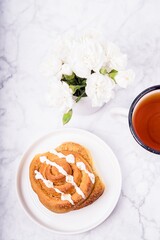 Homemade cinnamon bun on white plate and black tea on the white marble background. Flat lay