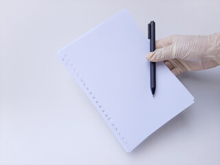 A hand with white latex glove holds a black pen and blank white paper. Isolated on a white background, side view