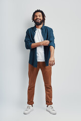 Full length of handsome young African man in casual wear adjusting sleeve and smiling while...