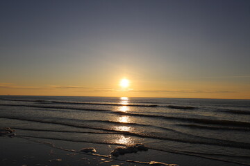 Beautiful warm golden sunlit clouds during sunset perfectly reflecting in the sand on a beach.